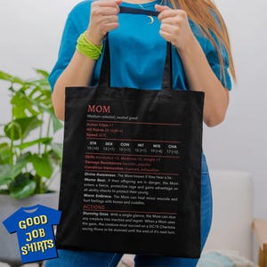 May include: Black tote bag with a white graphic of a character sheet for a "MOM" character. The character sheet includes stats like strength, dexterity, constitution, intelligence, wisdom, and charisma. The text "GOOD JOB SHIRTS" is printed in white on a red background in the lower left corner of the bag.