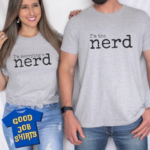 May include: A couple wearing matching gray t-shirts with a playful message. The woman's shirt says "I'm marrying a nerd" and the man's shirt says "I'm the nerd".