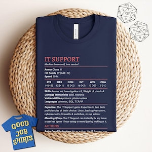 May include: Dark blue t-shirt with pink text reading "IT SUPPORT" and a character sheet design. Includes stats and skills. A small blue shirt with "GOOD JOB SHIRTS" is in the corner.