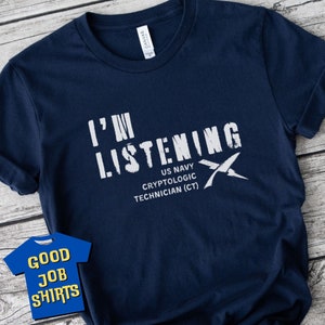 May include: A navy blue t-shirt with white text that reads "I'm Listening" with a white graphic of a crossed out X. Below the text is "US Navy Cryptologic Technician (CT)".