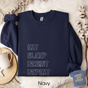 May include: A white ceramic mug with a black handle and the text "But First, Coffee" in a black, handwritten-style font. The mug is on a white surface.