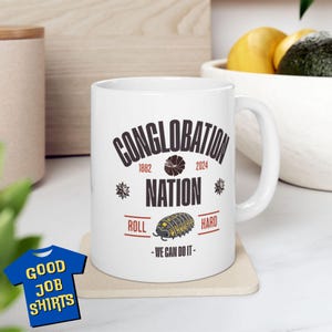 May include: White ceramic mug with a black and white graphic design featuring a pill bug and the text "Conglobation Nation 1882 2024 Roll Hard - We Can Do It - "