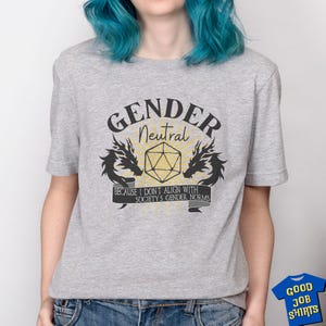May include: Gray t-shirt with a black and yellow graphic design. The graphic features a 20-sided die, two dragons, and the text "Gender Neutral" and "Because I don't align with society's gender norms".