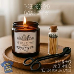 May include: A three-piece DND candle gift set. The set includes a lit 4oz soy wax jar candle, a jar of matches, and a wick trimmer. The candle label reads "Smells Like The Tears of My Players."