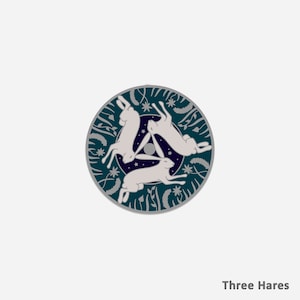 May include: A circular design featuring three white hares in a circle, with a dark blue background and white stars. The hares are in a triangular formation, with their heads facing the centre of the circle. The design is surrounded by a border of green leaves and flowers.