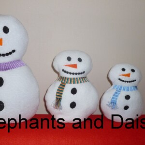 May include: Four white felt snowman ornaments of varying sizes. The largest snowman has a purple scarf, the next largest has a green and orange scarf, the next has a blue and white scarf, and the smallest has a red and white scarf. The text "Elephants and Daisy's" is visible at the bottom of the image.