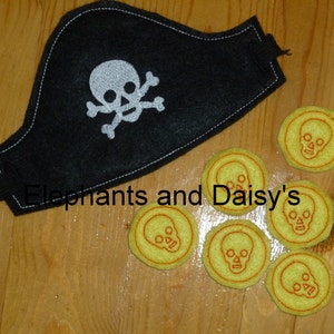 May include: A black felt pirate eye patch with a white skull and crossbones design.  There are seven yellow felt coins with a red outline and a white skull design on a wooden surface.