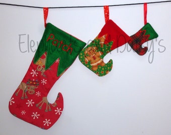 May include: Three Christmas stockings hanging on a string. The largest stocking is red with a white snowflake pattern and a green felt cuff with the name "Patch" embroidered on it. The middle stocking is green with a gingerbread man pattern and a red felt cuff. The smallest stocking is red with a plaid pattern and a green felt cuff.