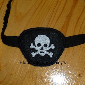 May include: Black eye patch with an embroidered white skull and crossbones design. The eye patch is attached to a black elastic strap.