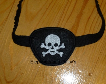 May include: Black eye patch with an embroidered white skull and crossbones design. The eye patch is attached to a black elastic strap.