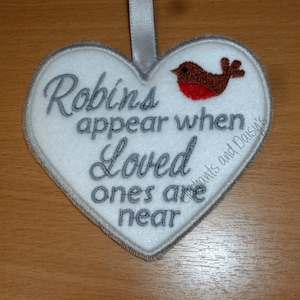 May include: White heart-shaped ornament with gray embroidered text that reads "Robins appear when loved ones are near" and a red robin with a brown body and gray wings.