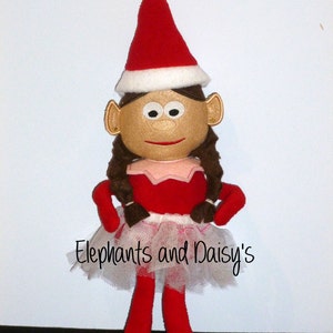 May include: A handmade doll with a red and white elf hat, brown hair, and a red outfit. The doll has a white tutu and the text "Elephants and Daisy's" is printed on the tutu.