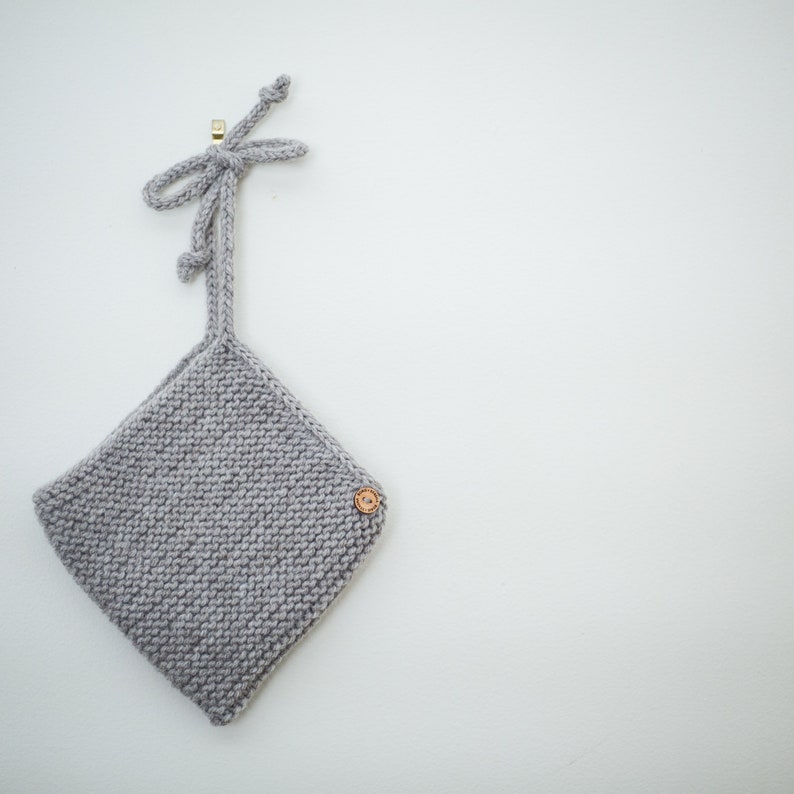 K&ouml;nnte beinhalten: Eine graue gestrickte Babyhaube mit einem Holzknopf und einer Schleife oben.