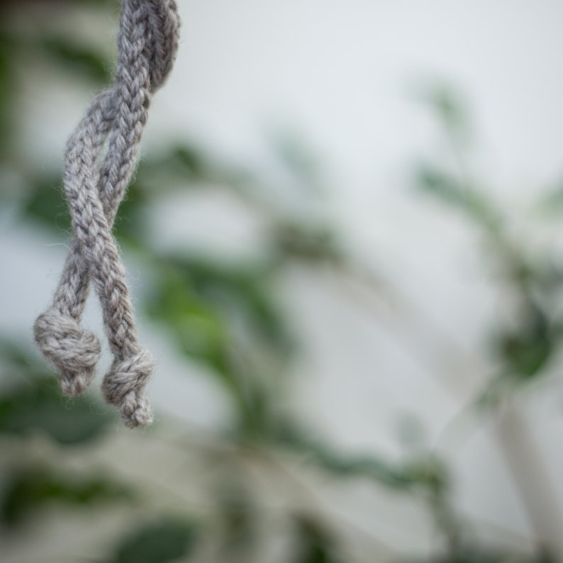 K&ouml;nnte beinhalten: Nahaufnahme eines grauen Seils mit einem Knoten am Ende. Das Seil h&auml;ngt vor einem verschwommenen Hintergrund aus gr&uuml;nem Laub.