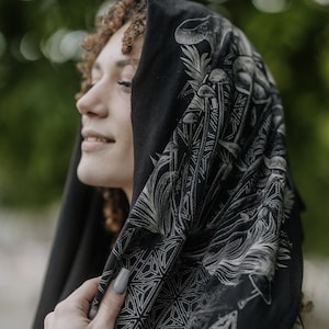 May include: A black hooded scarf with a white geometric and mushroom design. The scarf is made of a soft, comfortable fabric and is perfect for adding a touch of style to any outfit.