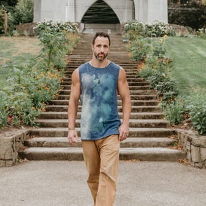 May include: A man wearing a blue tie-dye tank top and khaki pants walks down a set of stone steps. He is looking directly at the camera.