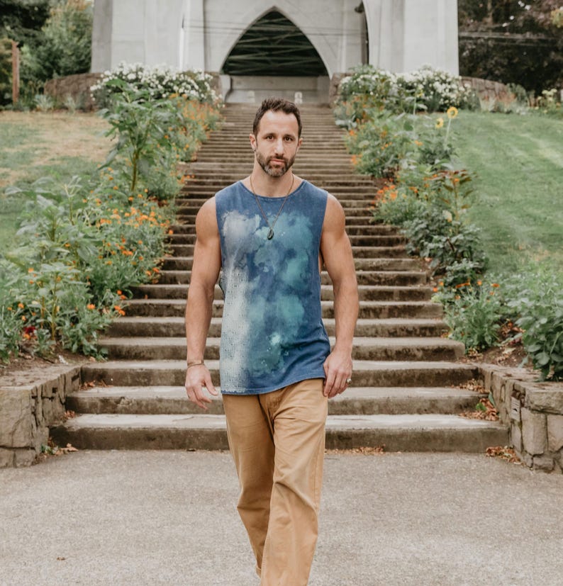 May include: A man wearing a blue tie-dye tank top and khaki pants walks down a set of stone steps. He is looking directly at the camera.