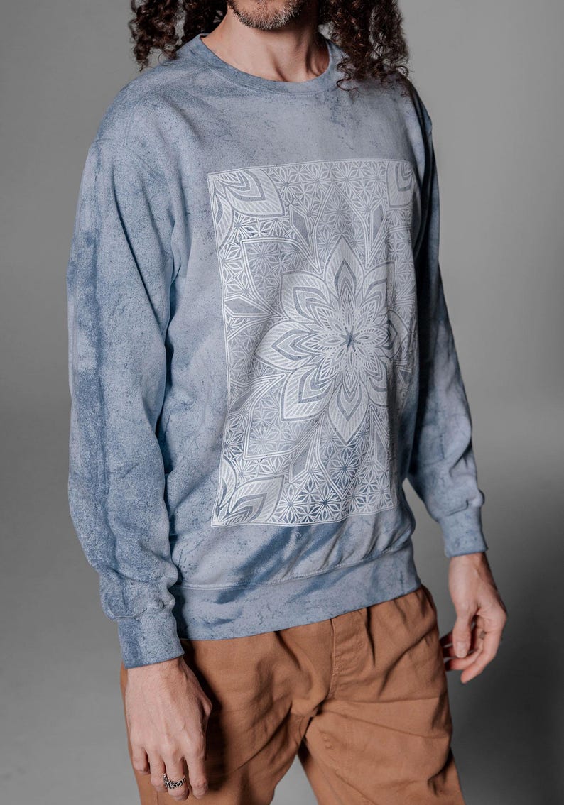 Pode incluir: Camisola azul tie-dye com um design floral de mandala branco na frente. A parte superior de manga comprida tem decote redondo. O modelo est&aacute; a usar cal&ccedil;as castanhas. O material parece macio.