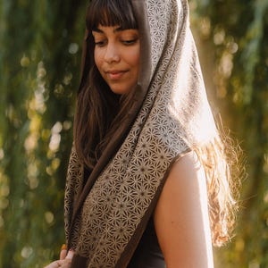 Peut inclure: Un foulard carr&eacute; pr&eacute;sentant une base marron fonc&eacute; avec un motif g&eacute;om&eacute;trique d'&eacute;toiles beige clair r&eacute;p&eacute;titif. Le tissu est drap&eacute; sur la t&ecirc;te et les &eacute;paules, mettant en valeur un bord ourl&eacute; propre et un motif imprim&eacute; sym&eacute;trique et coh&eacute;rent.
