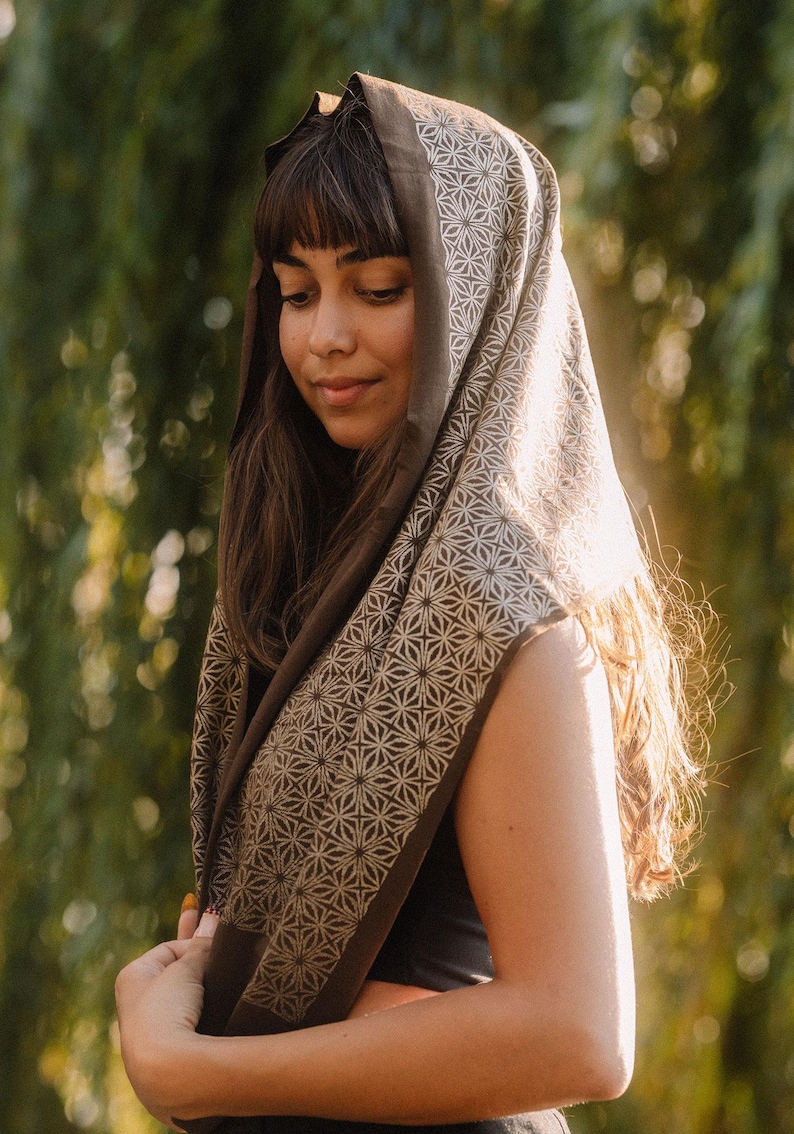 Peut inclure: Un foulard carr&eacute; pr&eacute;sentant une base marron fonc&eacute; avec un motif g&eacute;om&eacute;trique d'&eacute;toiles beige clair r&eacute;p&eacute;titif. Le tissu est drap&eacute; sur la t&ecirc;te et les &eacute;paules, mettant en valeur un bord ourl&eacute; propre et un motif imprim&eacute; sym&eacute;trique et coh&eacute;rent.