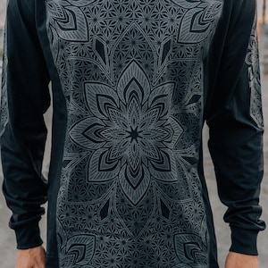 May include: Black long-sleeved shirt with a large, intricate grey floral mandala design on the front. The sleeves also have a smaller, repeating pattern. The shirt is made of a soft, dark material.