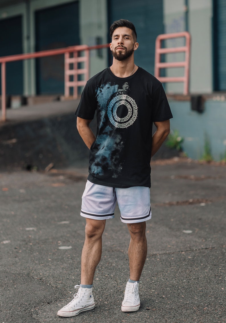 May include: A person wearing a black t-shirt with a blue and white circular design, white basketball shorts, and white sneakers.