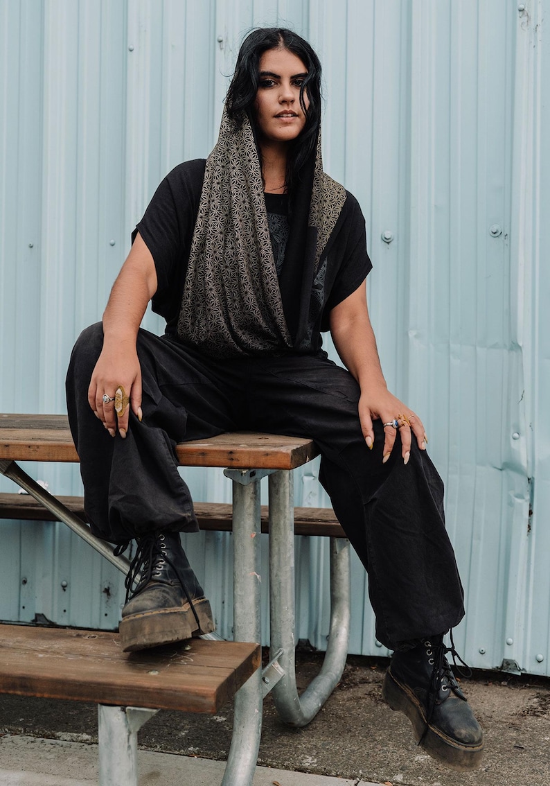 Peut inclure: Un capuchon noir orn&eacute; d'un motif g&eacute;om&eacute;trique d'&eacute;toiles dor&eacute;es r&eacute;p&eacute;titives, port&eacute; sur un t-shirt noir &agrave; manches courtes et un pantalon noir &agrave; jambes larges. La tenue est compl&eacute;t&eacute;e par des bottines noires &agrave; lacets et plusieurs bagues.