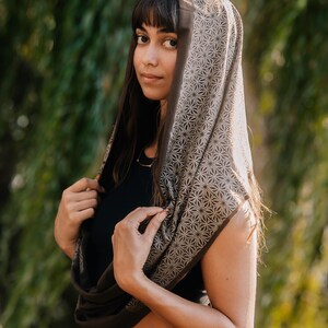 Peut inclure: Une &eacute;charpe infinie marron fonc&eacute; orn&eacute;e d'un motif g&eacute;om&eacute;trique en forme d'&eacute;toile r&eacute;p&eacute;titif dans une teinte beige plus claire. L'&eacute;charpe est drap&eacute;e sur la t&ecirc;te et autour du cou, mettant en valeur une texture de tissu douce et un imprim&eacute; complexe.