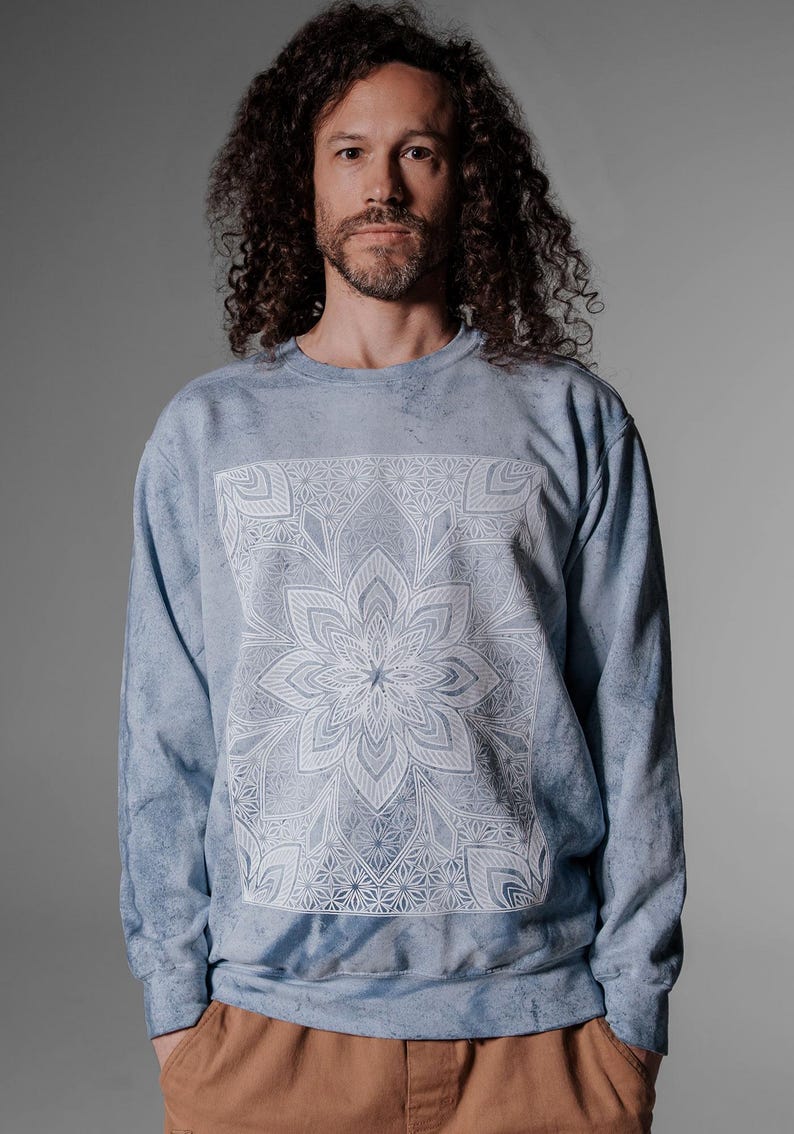 Pode incluir: Camisola azul clara com um design de mandala floral branco. A parte superior de manga comprida tem um efeito tie-dye e gola redonda. O gr&aacute;fico est&aacute; centrado na frente da pe&ccedil;a.