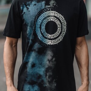 May include: Black t-shirt with a blue and white abstract design featuring a circular pattern of stylized text.