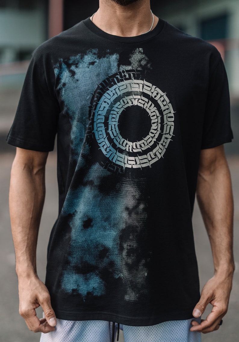 May include: Black t-shirt with a blue and white abstract design featuring a circular pattern of stylized text.