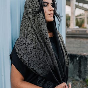 Peut inclure: Une capuche noire avec un motif g&eacute;om&eacute;trique d'&eacute;toiles r&eacute;p&eacute;titif dans un ton dor&eacute; att&eacute;nu&eacute;. Le tissu se drape sur la t&ecirc;te et les &eacute;paules, mettant en valeur un imprim&eacute; de g&eacute;om&eacute;trie sacr&eacute;e d&eacute;taill&eacute; sur la capuche et une section noire unie.