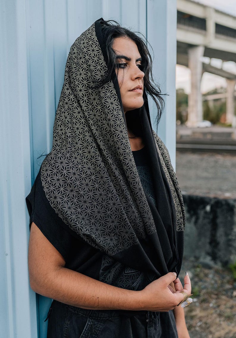 Peut inclure: Une capuche noire avec un motif g&eacute;om&eacute;trique d'&eacute;toiles r&eacute;p&eacute;titif dans un ton dor&eacute; att&eacute;nu&eacute;. Le tissu se drape sur la t&ecirc;te et les &eacute;paules, mettant en valeur un imprim&eacute; de g&eacute;om&eacute;trie sacr&eacute;e d&eacute;taill&eacute; sur la capuche et une section noire unie.