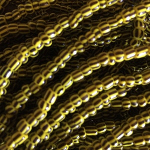 May include: A close-up of a strand of yellow and black striped beads. The beads are small and round, and they are strung together in a long strand.