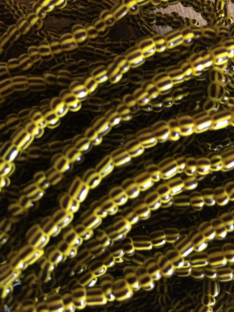May include: A close-up of a strand of yellow and black striped beads. The beads are small and round, and they are strung together in a long strand.