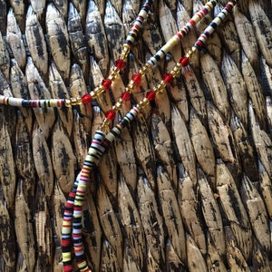 May include: A multi-strand beaded necklace with red, white, black, and yellow beads. The necklace also features clear and gold beads.