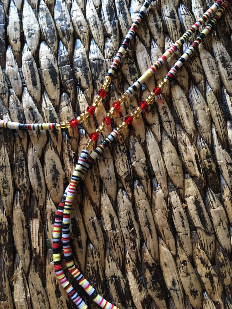 May include: A multi-strand beaded necklace with red, white, black, and yellow beads. The necklace also features clear and gold beads.
