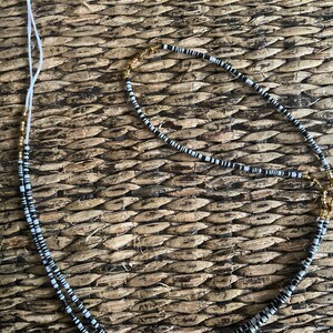 May include: A black and white beaded necklace with gold accents. The necklace is made of small, round beads and is strung on a white cord.