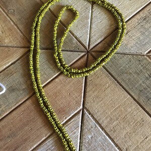 May include: A yellow and black beaded necklace with a white string attached.