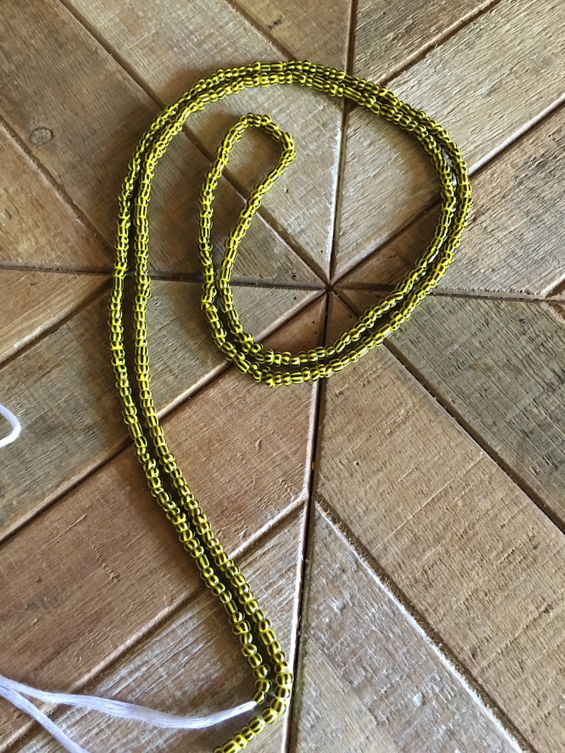 May include: A yellow and black beaded necklace with a white string attached.