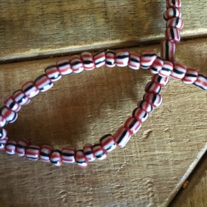 May include: A close-up of a red, white, and black beaded necklace. The beads are small and round, and they are strung together in a repeating pattern.