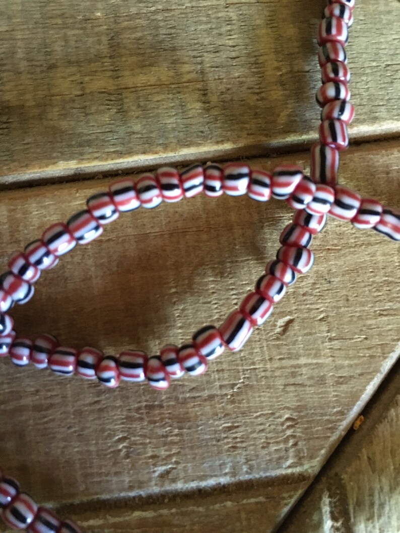 May include: A close-up of a red, white, and black beaded necklace. The beads are small and round, and they are strung together in a repeating pattern.