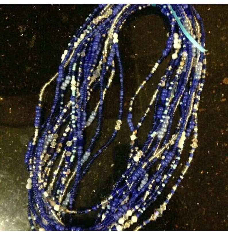 May include: A collection of beaded strands in shades of blue, silver, and white. The beads vary in size and shape, creating a textured appearance. The strands are tied together with a light blue ribbon. The beads are likely used for jewelry or craft projects.