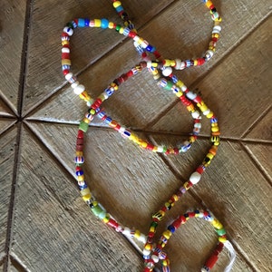 May include: A colorful beaded necklace with red, yellow, blue, white, and green beads. The necklace is made of glass beads and is strung on a white cord.