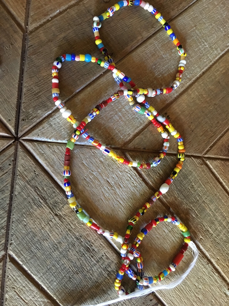 May include: A colorful beaded necklace with red, yellow, blue, white, and green beads. The necklace is made of glass beads and is strung on a white cord.