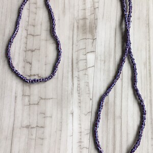 May include: A long, beaded necklace with a white tassel. The beads are a mix of purple and white.