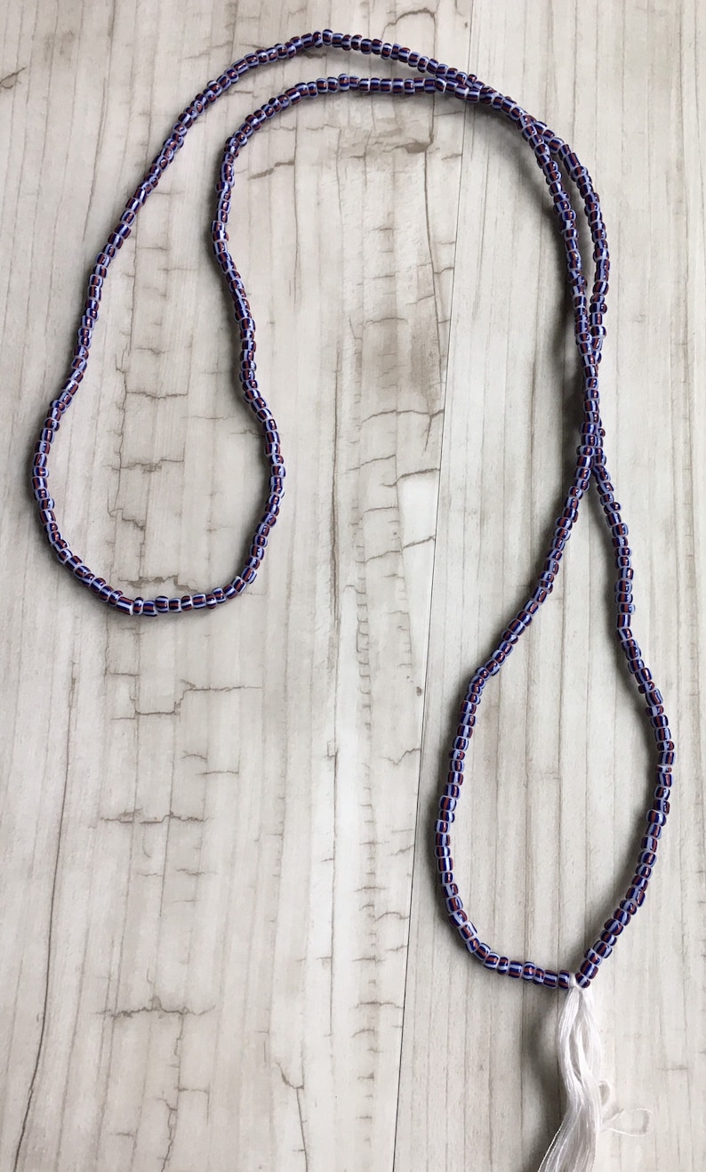 May include: A long, beaded necklace with a white tassel. The beads are a mix of purple and white.