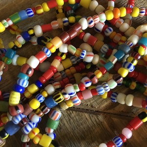 May include: A close-up of a pile of colorful glass beads. The beads are in various shapes and sizes, and they are strung together in a variety of patterns. The beads are a mix of red, yellow, blue, green, and white.