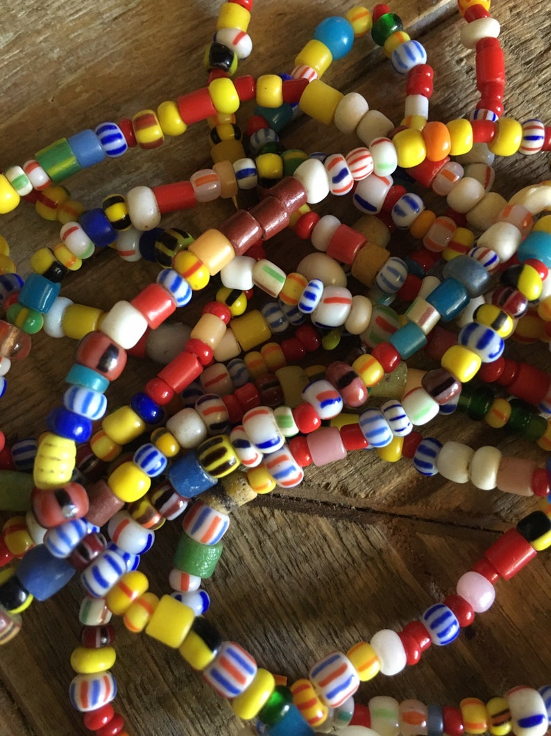 May include: A close-up of a pile of colorful glass beads. The beads are in various shapes and sizes, and they are strung together in a variety of patterns. The beads are a mix of red, yellow, blue, green, and white.