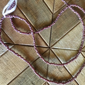 May include: A strand of red, white, and black beads. The beads are small and round, and they are strung together on a thin cord.